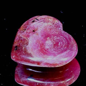 May include: A heart-shaped pink ruby gemstone with a swirling pattern. The gemstone is polished and has a glossy finish.