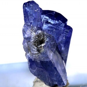 May include: A cluster of deep blue, faceted, translucent, rough-cut, natural zultanite gemstones. The crystals are clustered together in a random, organic formation.