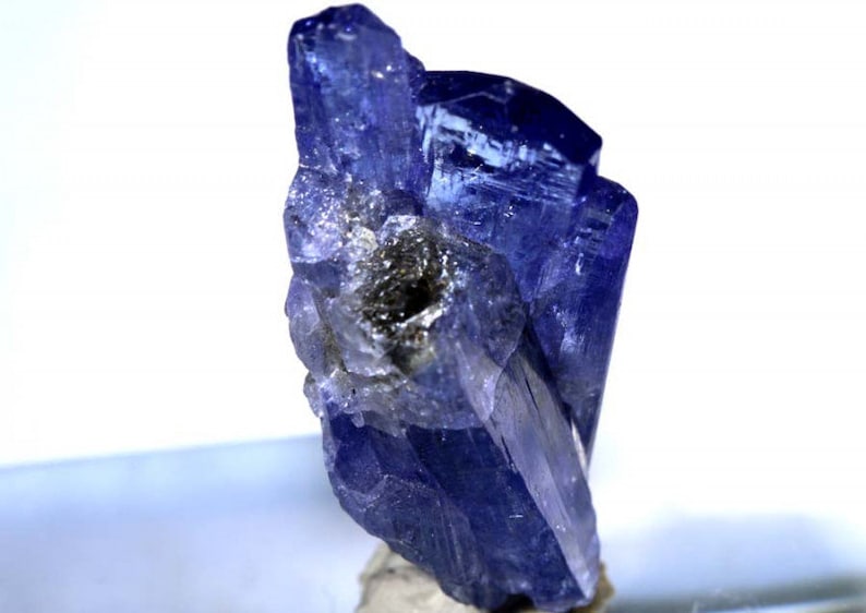May include: A cluster of deep blue, faceted, translucent, rough-cut, natural zultanite gemstones. The crystals are clustered together in a random, organic formation.