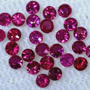 May include: A collection of loose, round, red gemstones. The gemstones are of various sizes and have a shiny, polished finish.