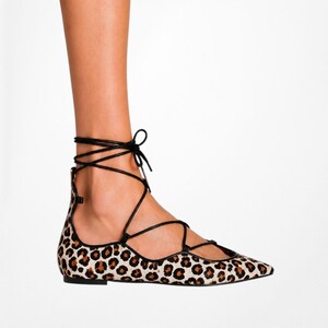 May include: Leopard print ballet flats with black laces that wrap around the ankle. The flats have a pointed toe and a low heel. The shoe's pattern is a mix of tan, brown, and black spots.