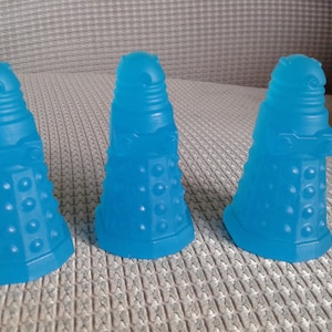 May include: Three blue plastic figurines of the Daleks from the Doctor Who television series. The Daleks are standing on a light grey surface.