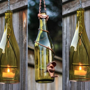 May include: Three glass wine bottles with copper wire wrapped around them, hanging from chains. Each bottle has a small candle inside and a metal ring around the top. The bottles are lit and the flames are visible.