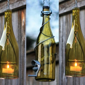May include: Three glass wine bottles with wire wrapped around them, hanging from chains. Each bottle has a candle inside and is lit. The bottles are a light green color.