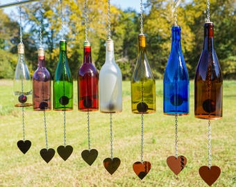 May include: A wind chime made from recycled wine bottles with heart-shaped metal chimes. The bottles are in various colors, including clear, red, green, yellow, blue, and brown.