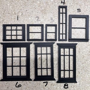 May include: A collection of eight black miniature window frames of varying rectangular shapes and grid patterns, labeled with handwritten numbers one through eight. Each frame features a distinct pane configuration, ranging from simple squares to tall, multi-paned designs, all crafted with a consistent matte black finish.