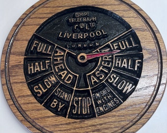 May include: A circular wooden wall plaque featuring a carved ship telegraph dial. The black center displays the text SHIP TELEGRAPH CO LTD LIVERPOOL LONDON, with settings for FULL, HALF, SLOW, STAND BY, STOP, AHEAD, ASTERN, and FINISHED WITH ENGINES.