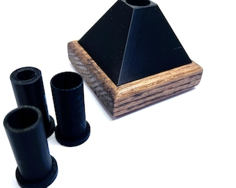 May include: A black pyramid-shaped object with a wooden base and three black cylindrical inserts. The pyramid has a hole at the top. The wooden base has a natural wood grain.