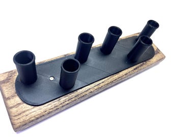 May include: A wooden knife block with six black cylindrical holders. The block has a rectangular wooden base with a dark gray, oval-shaped insert that holds the knife slots. The wood has a natural grain pattern.