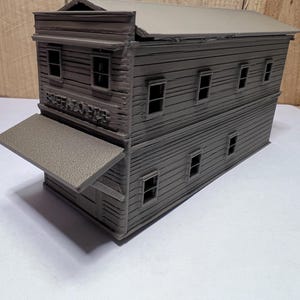 May include: A gray model of a two-story building with a flat roof and multiple windows. The building has a sign that reads "BUFFALO HUB". The model has a small awning extending from the front.