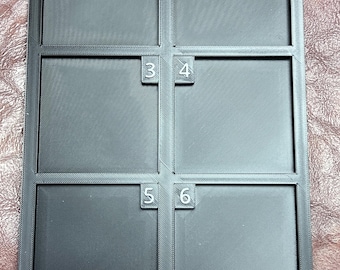 May include: A rectangular black tray featuring six individual square compartments arranged in two columns and three rows. Each compartment is labeled with a raised white number from one to six, positioned in the top corner of each square section.