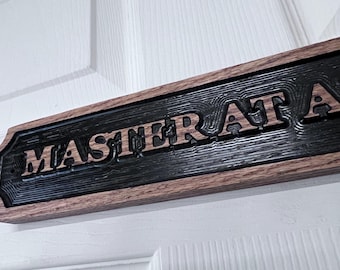 May include: Wooden sign with the words "MASTER AT" carved into the surface. The sign has a dark, textured background and a brown wooden frame. The sign is mounted on a white door.