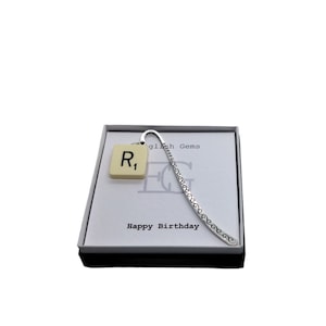 May include: A silver bookmark with a white tile featuring the letter "R" and the number "1". The bookmark is in a white box with the text "English Gems" and "Happy Birthday".