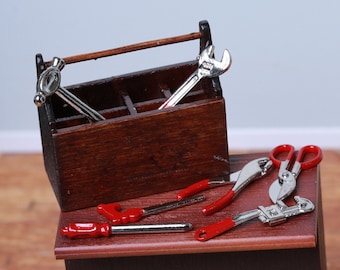 May include: A wooden toolbox with a metal wrench, a hammer, and a pair of pliers. The toolbox is open and the tools are spilling out.