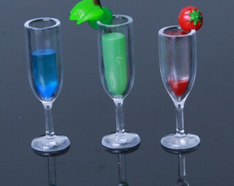 May include: Three clear glass cocktail glasses with different coloured liquids. The glass on the left has blue liquid, the middle glass has green liquid, and the glass on the right has red liquid. Each glass has a small decorative item on top.