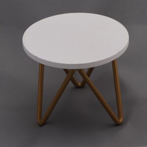 May include: A small white round table with a gold metal tripod base.