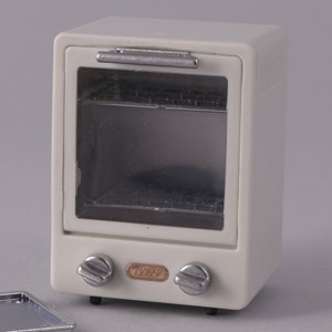 May include: White miniature oven with a glass door and two silver knobs. The oven has a silver handle and the word "TOAST" printed on the front.