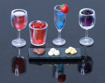 May include: A miniature set of four clear glass drinkware pieces, including a red wine glass, a blue cocktail glass, a purple wine glass, and a red juice glass. The set also includes a small black tray with three chocolate sweets and two white meringue cookies.