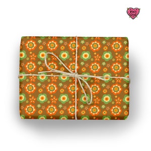 May include: A rectangular gift wrapped in brown paper featuring a repeating pattern of orange, light green, and yellow flowers. The package is tied with a thin, natural-colored jute twine string tied in a bow at the center. A small heart logo reads Pixie Drew.