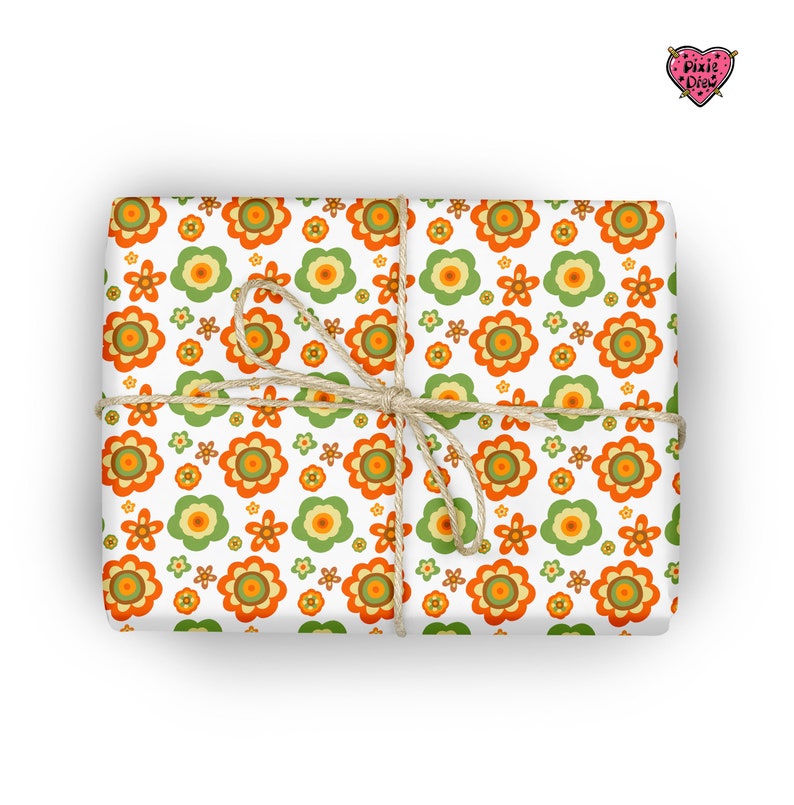 May include: A rectangular gift wrapped in white paper featuring a repeating pattern of orange, yellow, and green flowers. The package is tied with a thin, natural-colored jute twine string. A small heart-shaped logo with the text Pixie Drew is visible in the top right corner.