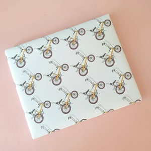 Op de afbeelding: Wit inpakpapier met een herhalend patroon van gele fietsen. De fietsen zijn getekend in een eenvoudige, cartoonachtige stijl.