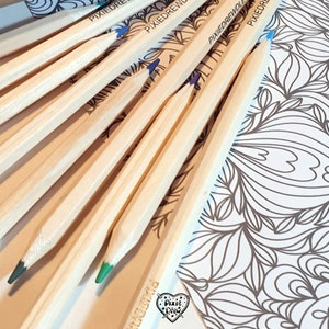 May include: A close-up of a set of wooden pencils with green and blue colored tips. The pencils are arranged in a fan shape on a white surface with a black and white patterned design. The pencils are labeled "PixieDrew".