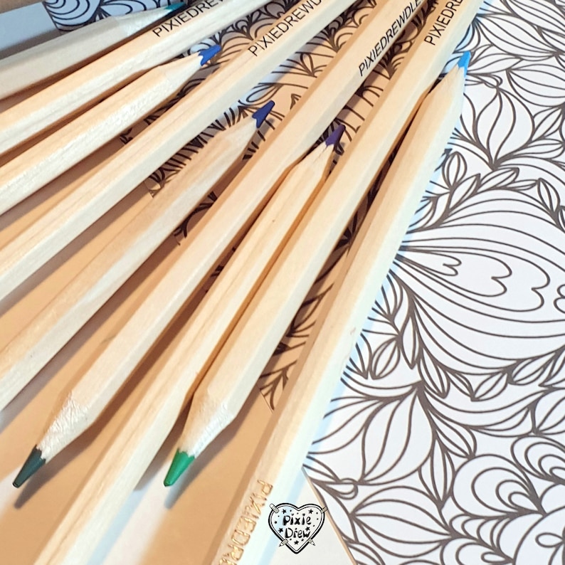 May include: A close-up of a set of wooden pencils with green and blue colored tips. The pencils are arranged in a fan shape on a white surface with a black and white patterned design. The pencils are labeled "PixieDrew".