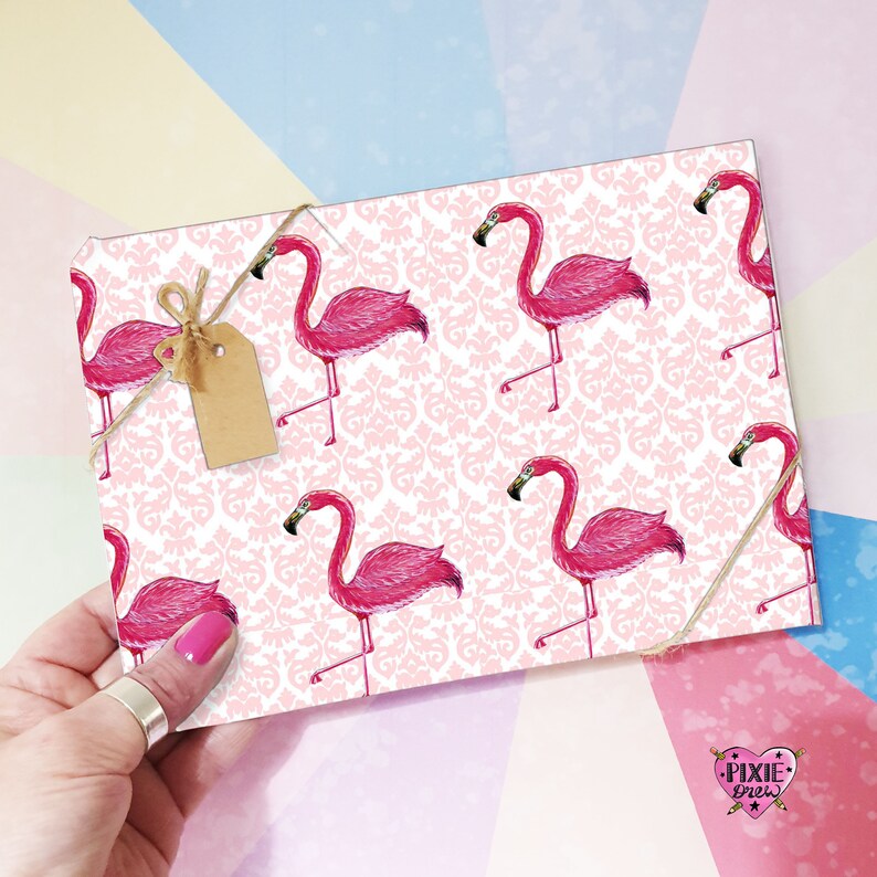 May include: Pink flamingo wrapping paper with a white damask pattern. The paper is wrapped around a gift box with a brown tag tied with twine.