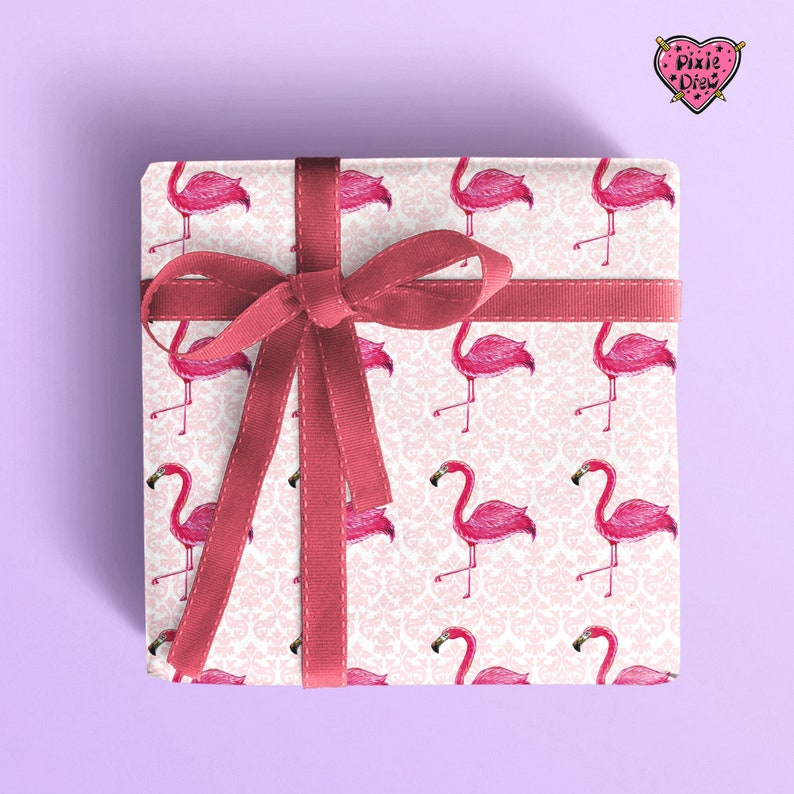 May include: A white gift box with a pink flamingo pattern and a red ribbon. The box is tied with a bow and has a pink damask pattern in the background.