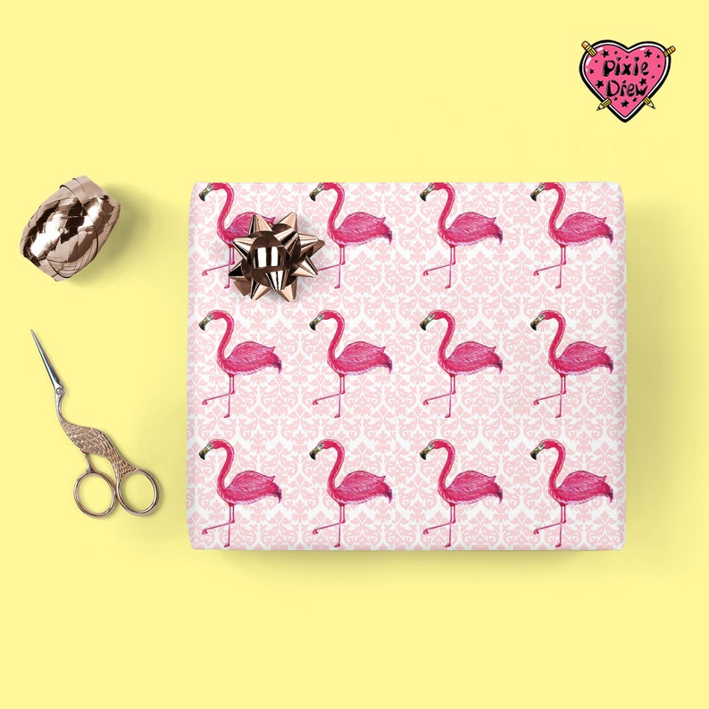 May include: Pink wrapping paper with a white damask pattern and pink flamingos. The paper has a heart-shaped logo with the text "Pixie Drew" in black and white.