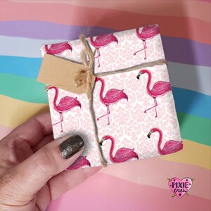 May include: Pink flamingo gift wrap with a white background and a damask pattern. The wrapping paper is tied with twine and a brown tag.
