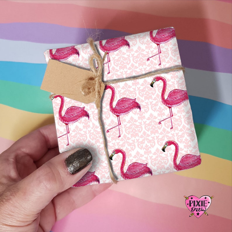 May include: Pink flamingo gift wrap with a white background and a damask pattern. The wrapping paper is tied with twine and a brown tag.