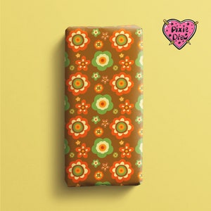 May include: A rectangular object wrapped in brown paper featuring a repeating pattern of orange, light green, and yellow flowers. In the top right corner, there is a pink heart-shaped logo with the text Pixie Drew written in black.