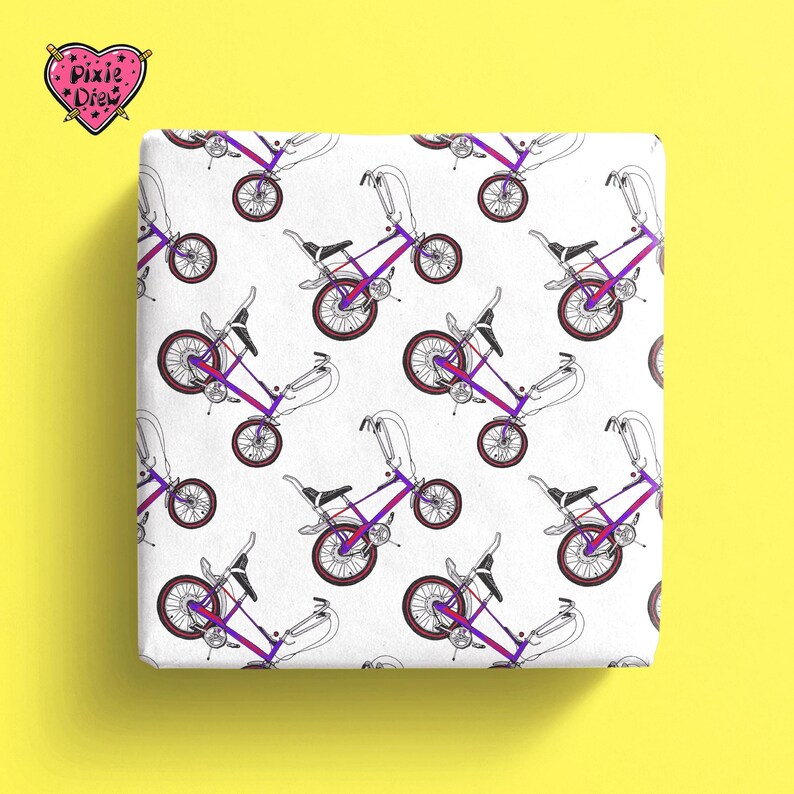 Op de afbeelding: Wit verpakkingspapier met een herhalend patroon van paarse en zwarte fietsen. De tekst "Pixie Drew" staat in een roze hart.