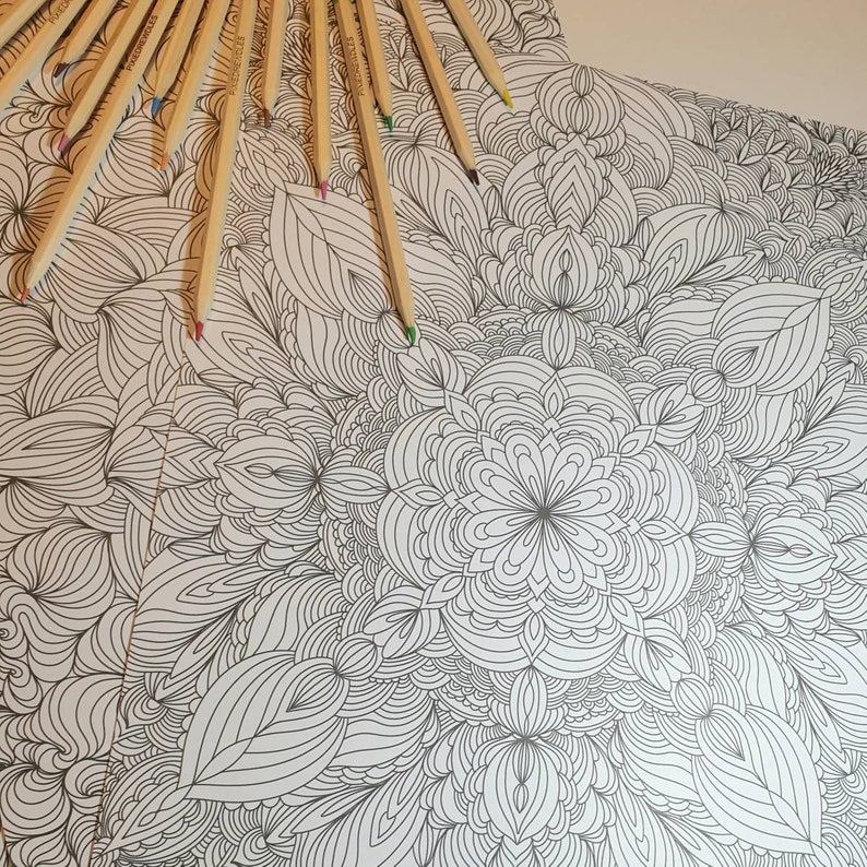 May include: A black and white intricate mandala design coloring book page with a variety of pencils laid out on top.