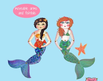 Puede incluir: Dos marionetas de sirenas con brazos y colas de pez móviles. Las sirenas tienen el pelo largo, una roja y otra marrón, y sostienen un pequeño pez naranja. Las sirenas están sobre un fondo azul claro con una estrella rosa y el texto "brazos móviles y colas de pez".
