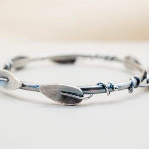 May include: A silver bangle bracelet with a twisted wire design and leaf-shaped accents.