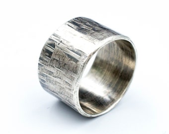 May include: A wide silver band ring with a textured, hammered finish. The ring is made of metal and has a polished interior.
