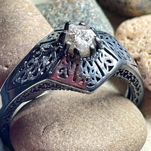 May include: A silver ring with a detailed filigree design and a clear, faceted gemstone in the center.