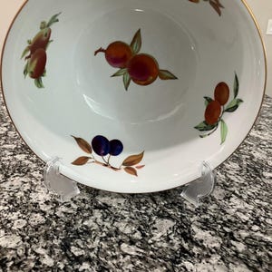 Pode incluir: Uma tigela de porcelana branca com uma borda dourada e um desenho de frutas. A tigela apresenta frutas vermelhas, laranja e roxas com folhas verdes.