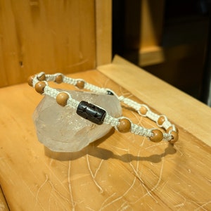 May include: A white cord bracelet with brown wooden beads and a black star-shaped bead.