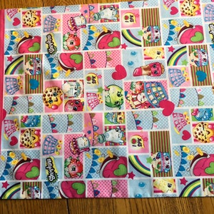 May include: A pink and blue fabric with a repeating pattern of cartoon characters, hearts, stars, and rainbows. The characters are all wearing different outfits and have different expressions. The fabric is made of cotton and is soft to the touch. The fabric is perfect for making pillows, blankets, and other home decor items.