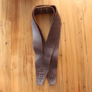 May include: Two brown leather straps with the text "646 WM" printed on them. The straps are tied together in a knot.