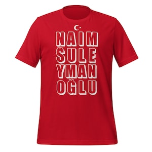 May include: Red t-shirt with white text that reads "NAIM SULE YMAN OGLU" and a small Turkish flag symbol above the text.
