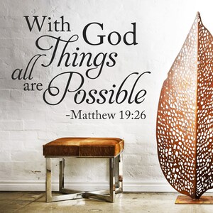 May include: A white brick wall with a black vinyl decal that reads "With God all things are possible - Matthew 19:26". A brown leather ottoman with a silver metal frame sits in front of the wall. A decorative metal leaf sculpture is on the right side of the image.