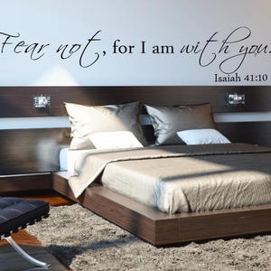 Puede incluir: Un dormitorio con una cama de madera y una cabecera acolchada. La cama está hecha con un edredón beige y dos almohadas. La pared sobre la cama tiene una calcomanía de vinilo negro con la cita "No temas, porque yo estoy contigo." y la referencia bíblica "Isaías 41:10".