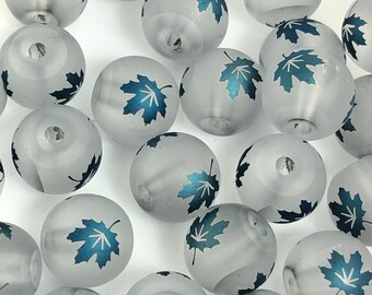 May include: A collection of frosted glass beads with a blue leaf design. The beads are round and have a hole in the center for stringing.