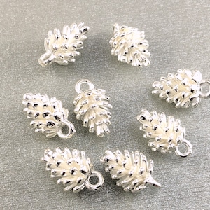 May include: Silver pine cone charms with a loop for hanging. The charms are detailed and have a textured surface.
