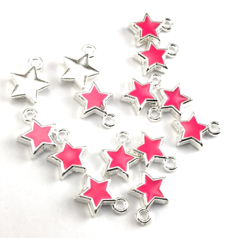 May include: A collection of silver-toned star-shaped charms with pink enamel. The charms have a loop at the top for attaching to jewelry or other crafts.