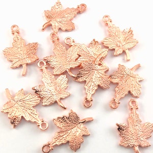 May include: A collection of 12 rose gold maple leaf charms with a loop for attaching to jewellery or other crafts.